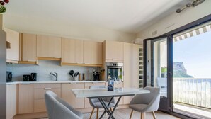 Eine moderne Küche mit hellen Holzschränken, einer weißen Arbeitsplatte und einem Essbereich mit Tisch und Stühlen.