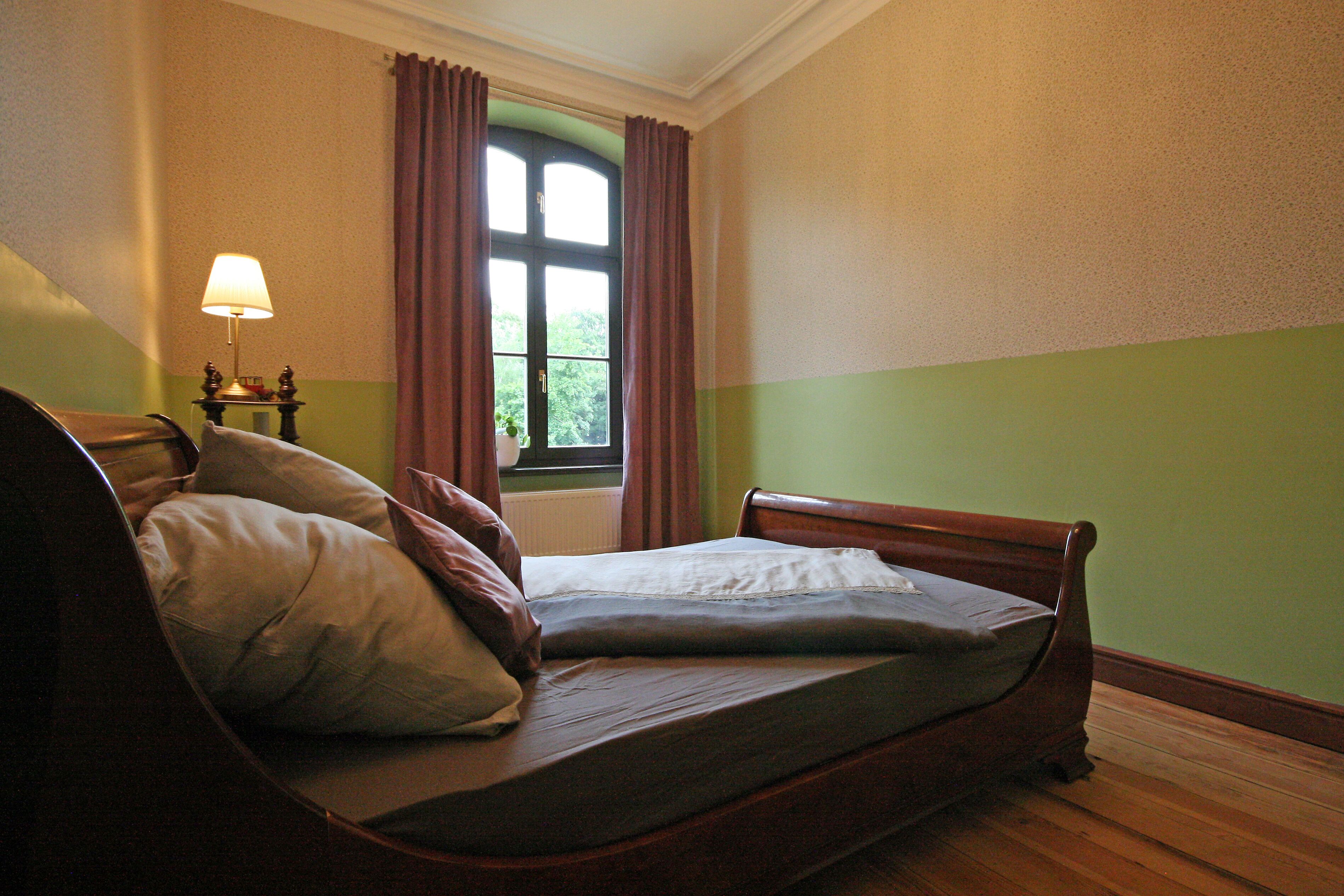 Un dormitorio con una cama individual, una mesita de noche con lámpara y una ventana con cortinas.