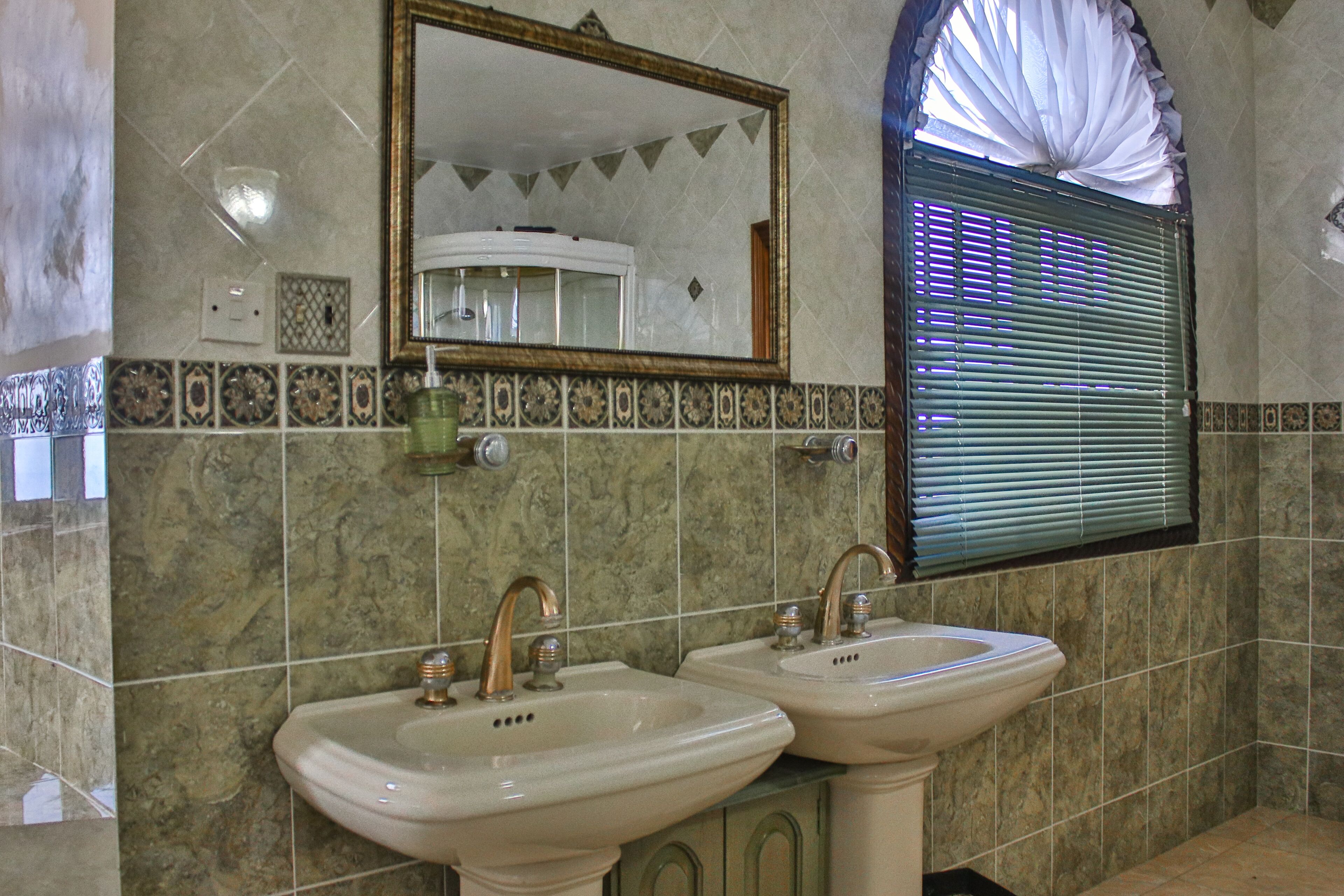 A bathroom with two sinks, a mirror, and a window with blinds.