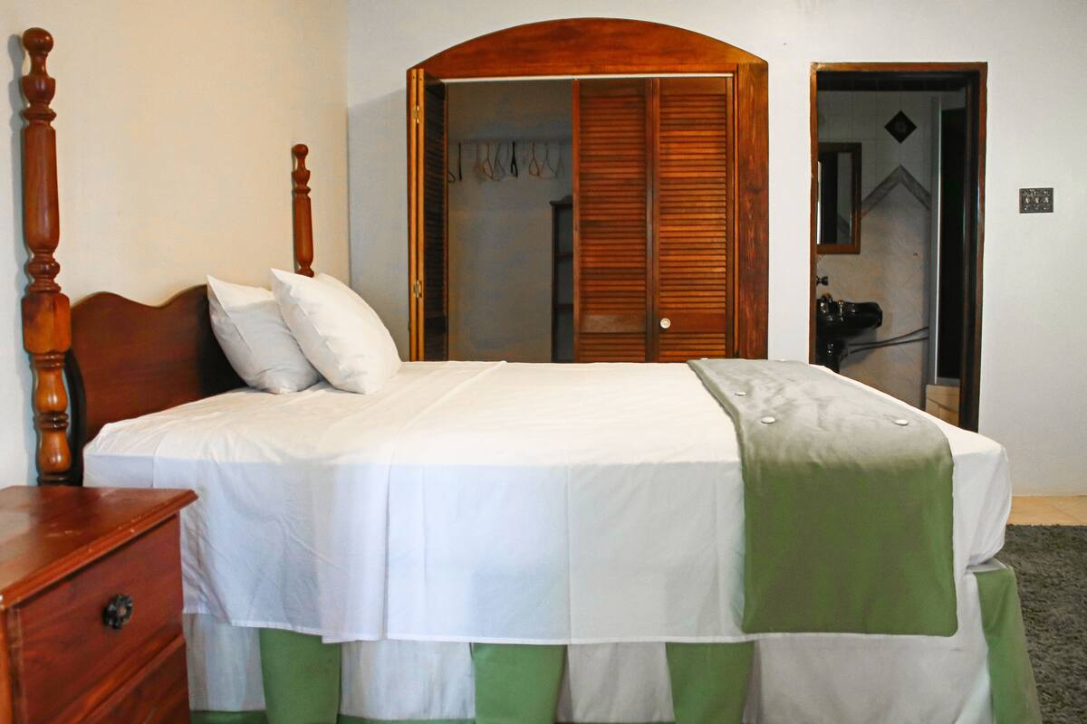 A bedroom with a wooden bed frame, white bedding, and a green and white bed skirt.
