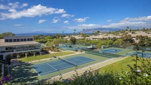 Un complejo de canchas de tenis con varias pistas, un edificio con amplios ventanales y un paisaje montañoso de fondo.