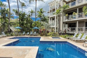 A swimming pool with lounge chairs and palm trees, surrounded by a multi-story building with balconies. - 125+ 5 STAR REVIEWS SAYS IT ALL! Upgraded thru/vaulted ceil/Golf & Ocean view! (Wailea)