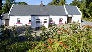 Une maison blanche avec un toit gris, entourée de verdure et de fleurs.