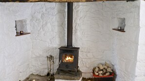 Une pièce aux murs de pierre, avec un poêle à bois, un feu de cheminée et une pile de bois de chauffage.