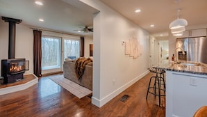 A modern kitchen with a stainless steel refrigerator, a bar area with stools, and a fireplace with a glass enclosure. - The Johnson Chalet in Bristol/Canandaigua*HOT TUB* (Canandaigua)