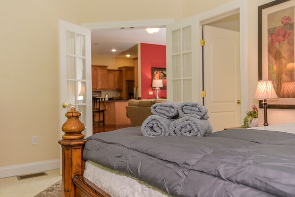 A bedroom with a bed, a wooden headboard, and a view into the kitchen. - Central to Mystic and Vineyards (Stonington)