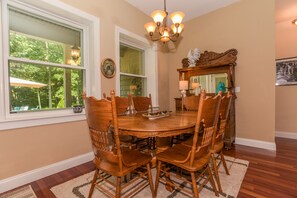 A dining room with a round wooden table surrounded by six chairs, a chandelier, and a mirror above the table.