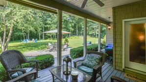 Une véranda aménagée avec des meubles en osier, une table en verre et une vue sur un jardin avec une pelouse, des chaises et un espace barbecue.