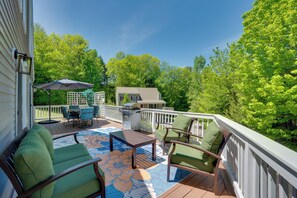 Une terrasse dotée de mobilier d’extérieur, d’un barbecue et offrant une vue sur une maison et des arbres.