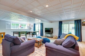 Amplia sala de estar con mesa de billar, asientos cómodos, televisor y ventanas grandes con cortinas.