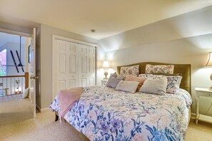 Une chambre avec une couvre-lit à motifs floraux, une tête de lit en bois, une table de chevet avec une lampe et une porte donnant sur un balcon où se trouvent des paires de skis.