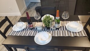 Una mesa de comedor dispuesta con platos blancos, dos copas de vino, una botella de vino, una vela y una pequeña planta en maceta.