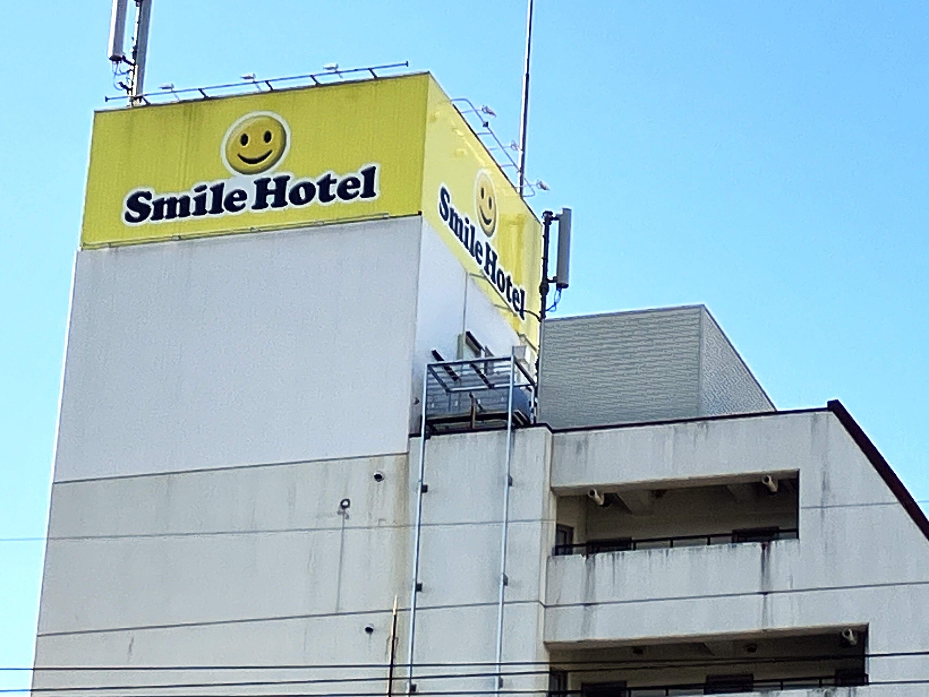 Un edificio con un gran letrero amarillo que dice "Smile Hotel" y un logotipo con una carita sonriente.