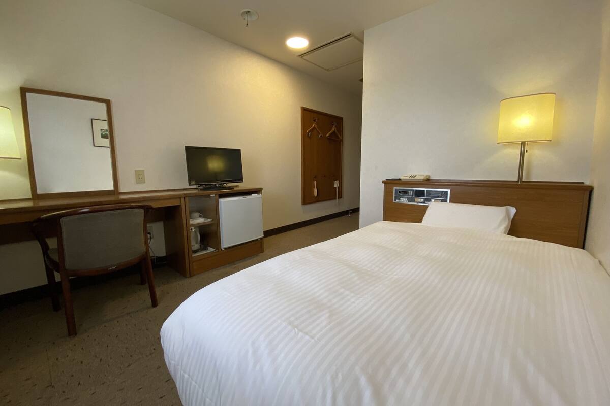 Une chambre d’hôtel comprenant un lit, un bureau avec une télévision, un réfrigérateur et une armoire.
