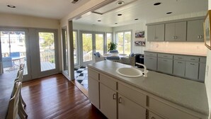 A modern kitchen with a large island, white cabinets, and a view to an outdoor patio. - Canal Front with Dock & Golf Cart, Family Friendly in South Litchfield (Pawleys Island)