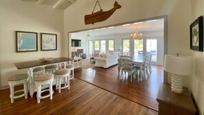A spacious living area with a wooden dining table, white chairs, and a hanging wooden sculpture. - Canal Front with Dock & Golf Cart, Family Friendly in South Litchfield (Pawleys Island)
