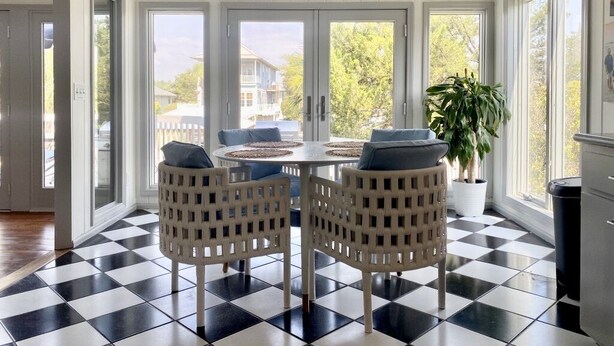 A sunroom with a checkered floor, a round table with chairs, and large windows offering a view of the outside. - Canal Front with Dock & Golf Cart, Family Friendly in South Litchfield (Pawleys Island)