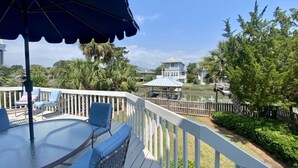 A deck with a table and chairs, a blue umbrella, and a view of a house and water. - Canal Front with Dock & Golf Cart, Family Friendly in South Litchfield (Pawleys Island)