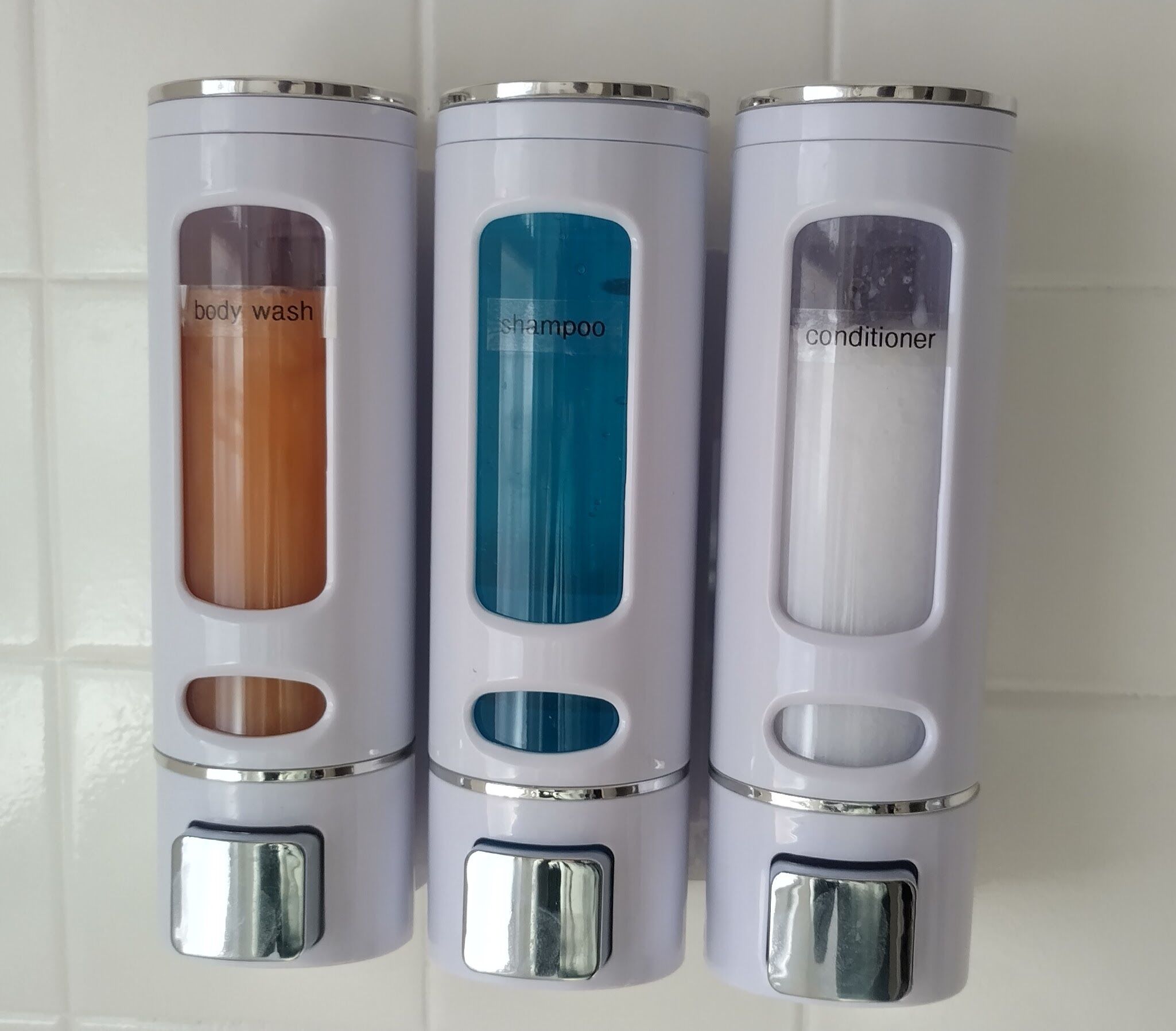 Drei weiße Spender mit Aufschriften für Duschgel, Shampoo und Conditioner.