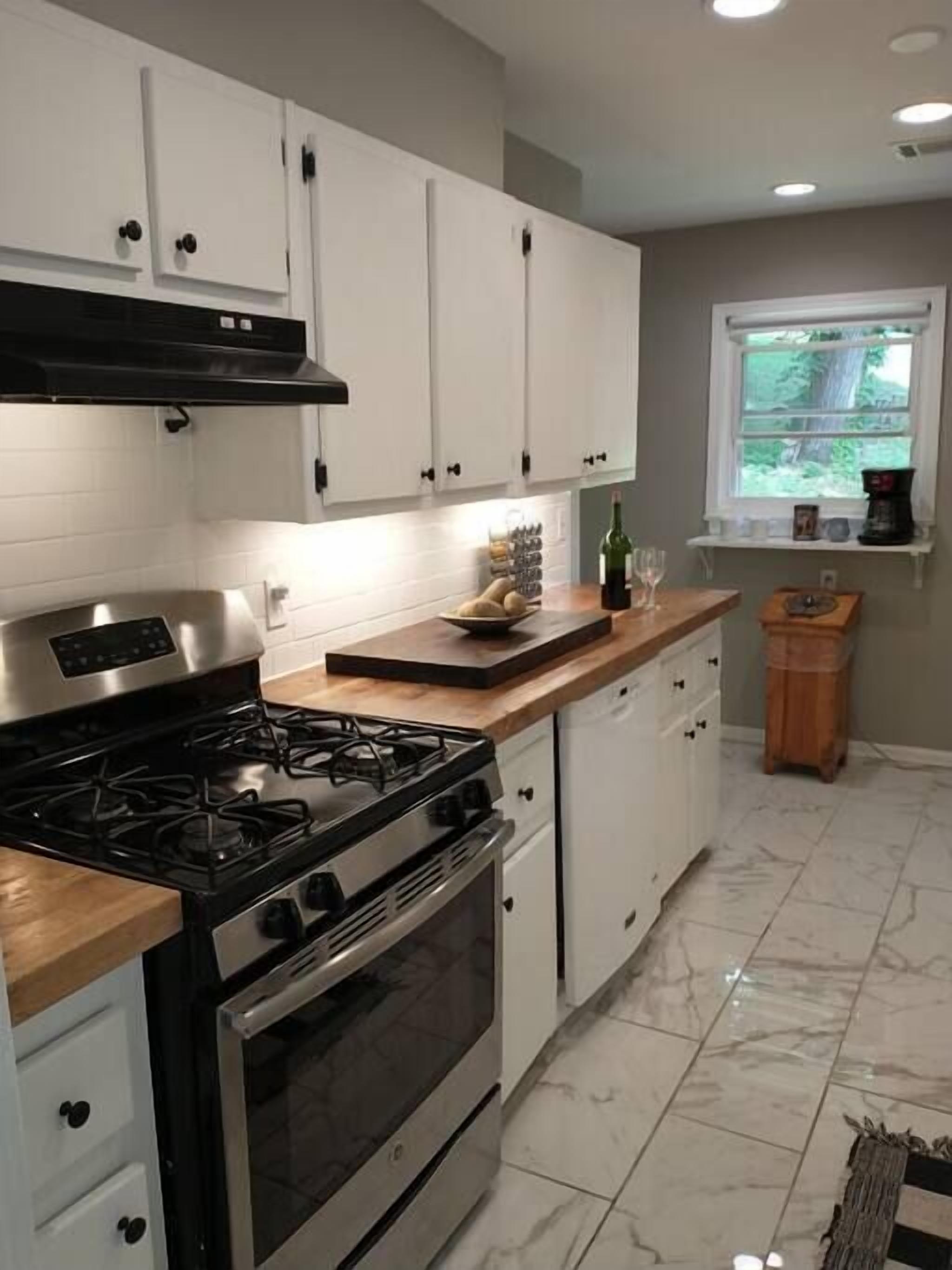 A modern kitchen with white cabinets, a stainless steel stove, and a marble floor.