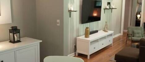 Una sala de estar moderna con un televisor de pantalla plana, muebles blancos y una lámpara colgante grande.