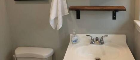A bathroom with a toilet, sink, and mirror. There is a framed picture on the wall and a towel hanging on a hook.