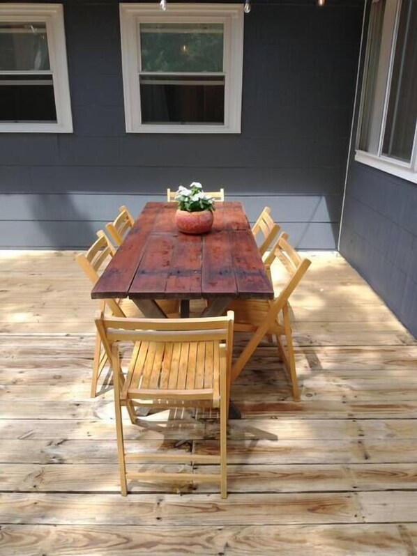 A wooden deck with a table and chairs, surrounded by a dark wall with windows.