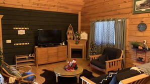 L’intérieur chaleureux d’un chalet avec une télévision, des meubles en bois, une cheminée et un sapin de Noël.
