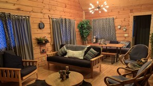 L’intérieur chaleureux d’un chalet avec un plancher en bois, un canapé, une table à manger et des chaises en osier.