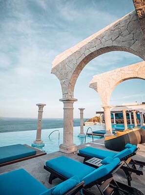 An infinity pool with blue lounge chairs, a stone archway, and a view of the sea. - 2 BR LUXURY VISTA IN RESORT RANKED #2 IN CABO SAN LUCAS (Cabo San Lucas)