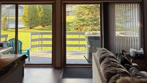 A cozy interior with a wooden ceiling, a sofa, and a view of a green outdoor area through large sliding glass doors.