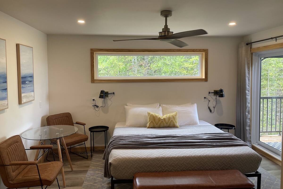 Een slaapkamer met een bed, plafondventilator, raam, tafel en stoelen.