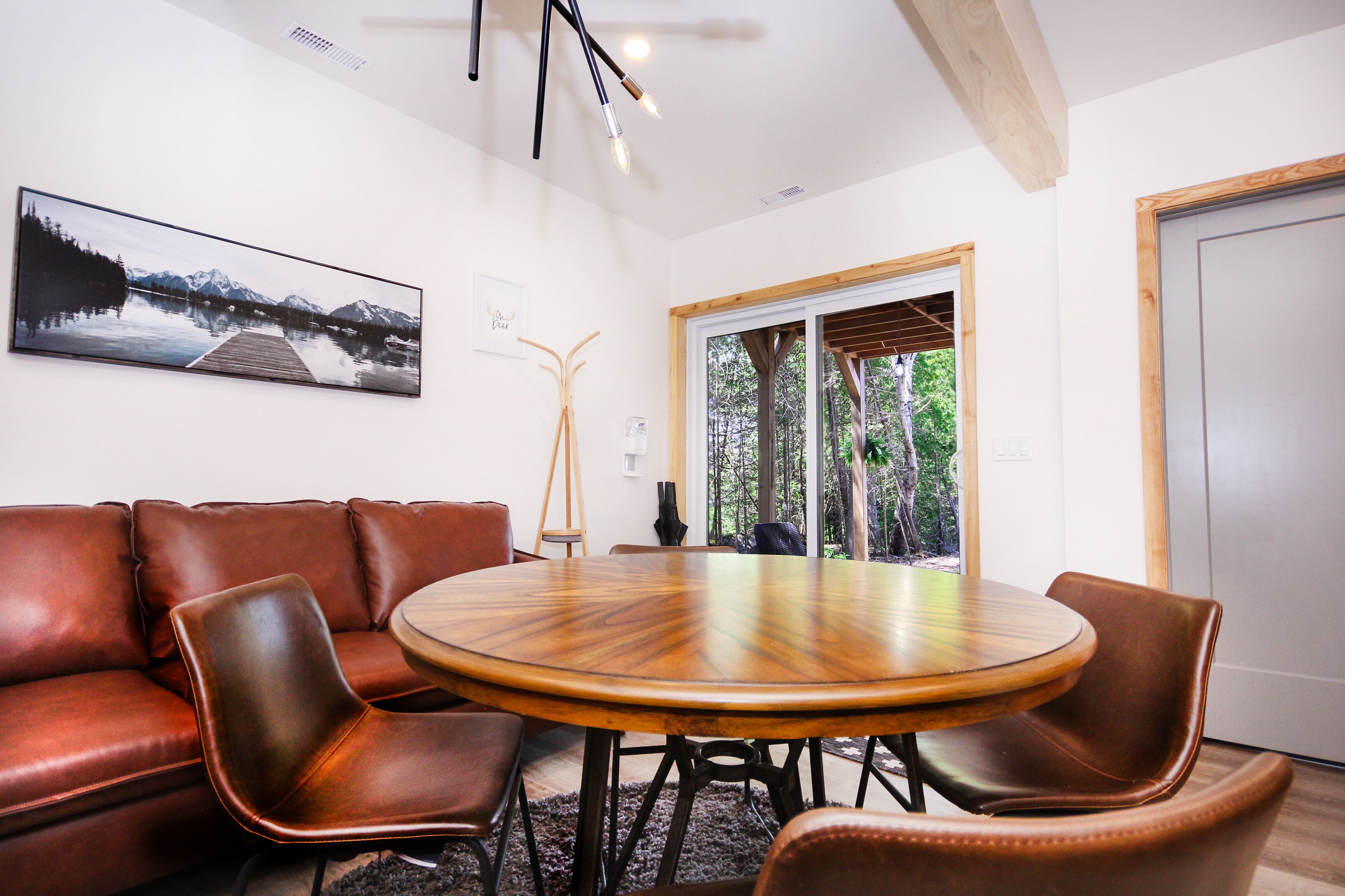 Un salón de conferencias con una mesa redonda de madera, sillas de cuero, un cuadro grande en la pared y vistas a árboles a través de una puerta de cristal.