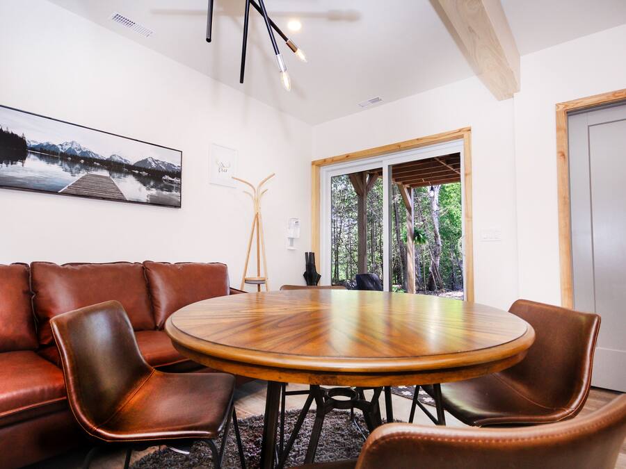 Un salón de conferencias con una mesa redonda de madera, sillas de cuero, un cuadro grande en la pared y vistas a árboles a través de una puerta de cristal.