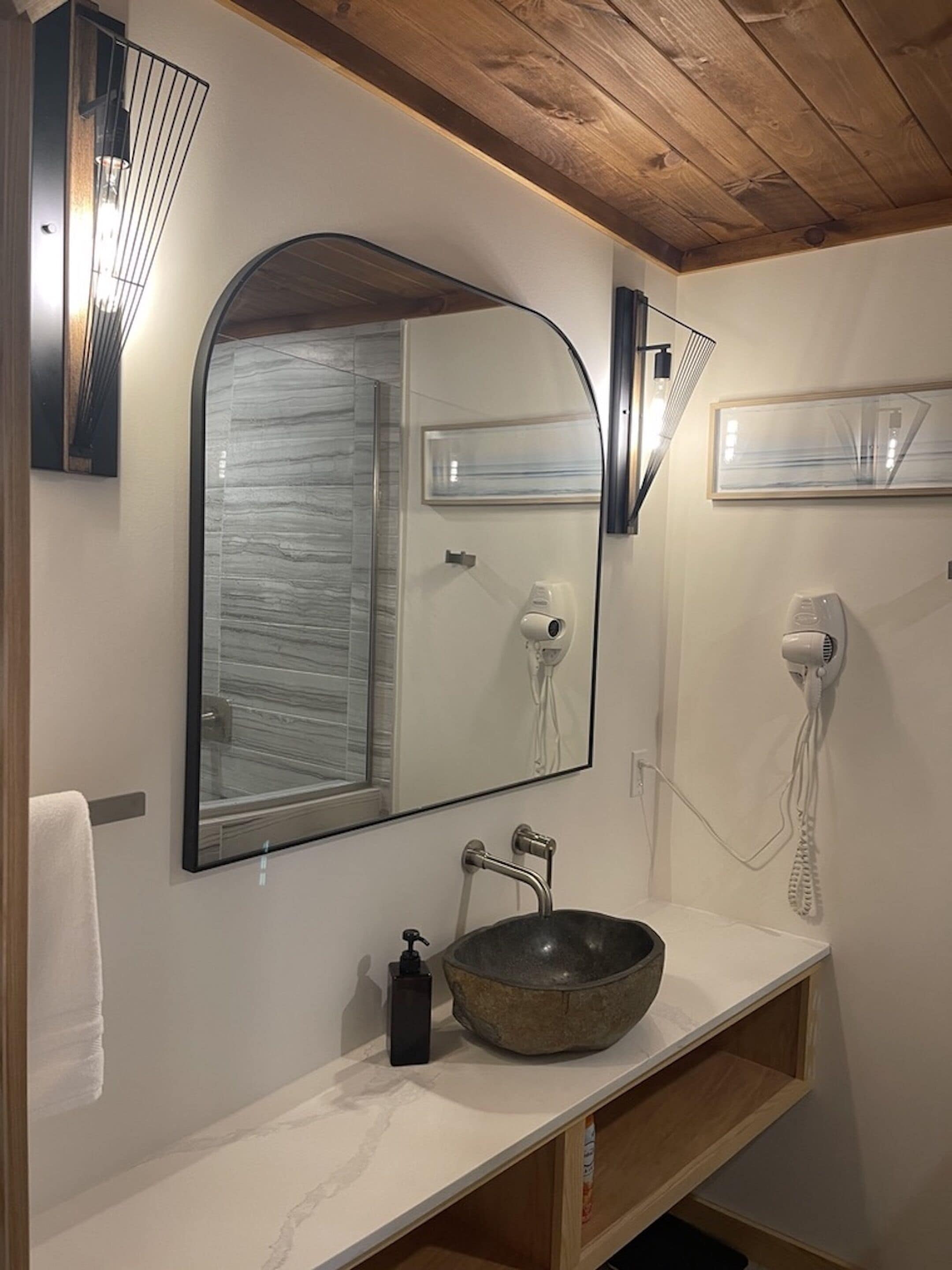 A bathroom with a large mirror, a stone sink, and a hairdryer mounted on the wall.