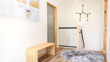 A hallway with wooden flooring, a bench, two round rugs, a painting, and a door.