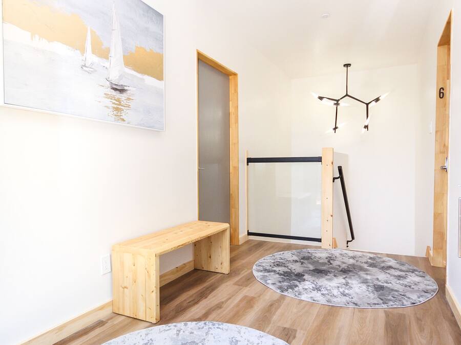 A hallway with wooden flooring, a bench, two round rugs, a painting, and a door.