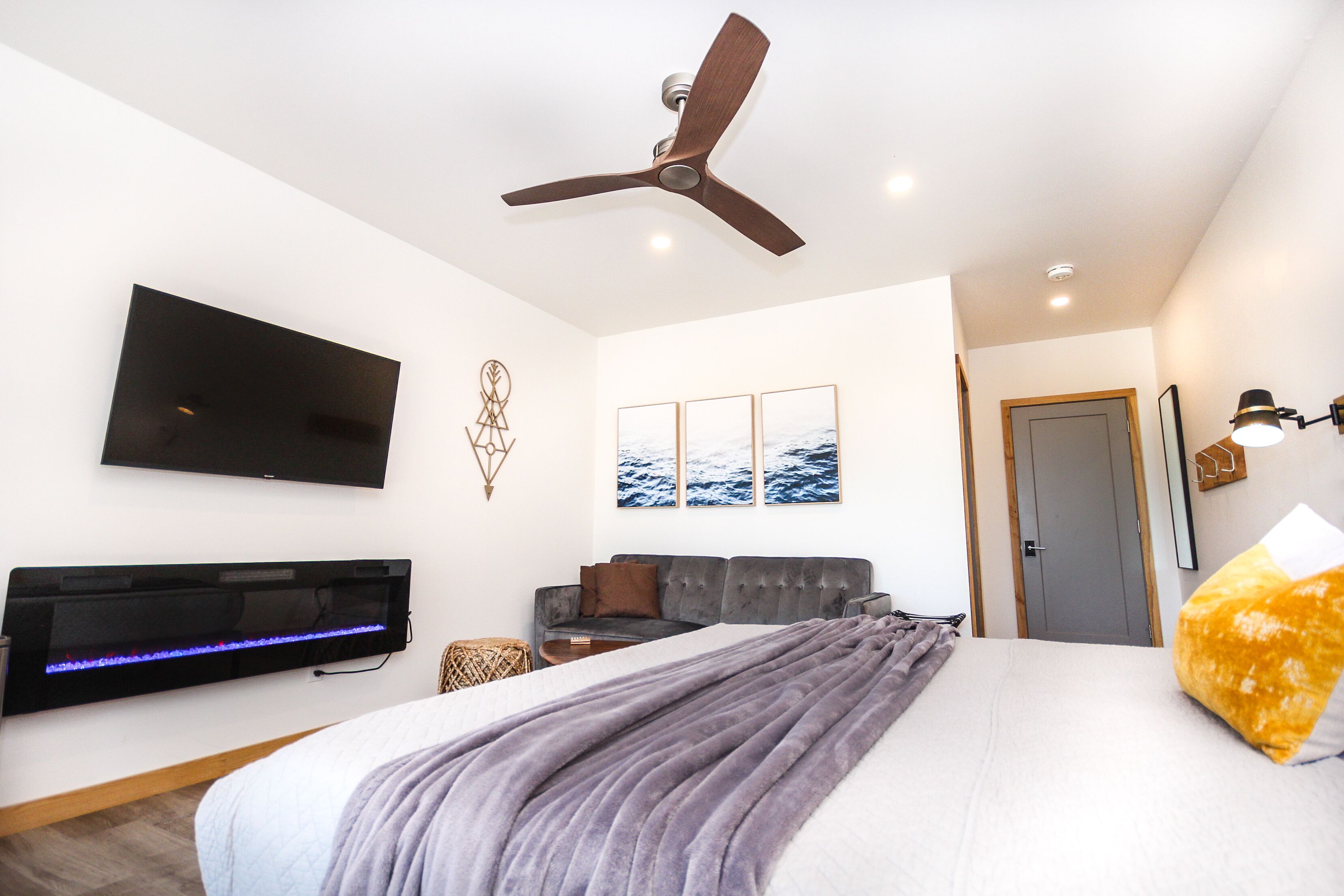 A modern bedroom with a bed, a flat-screen TV, a ceiling fan, and a wall-mounted heater.