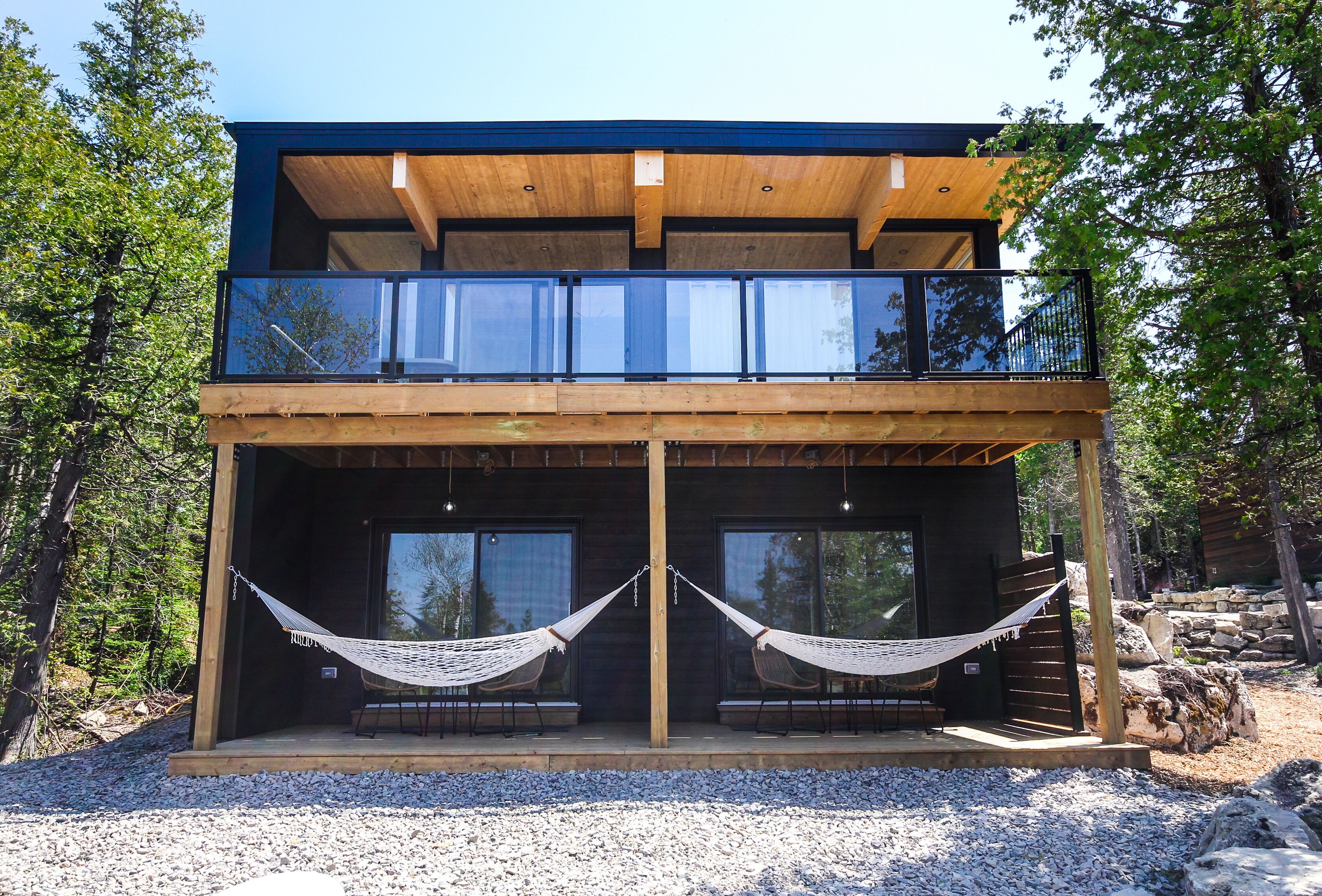 Eine moderne, zweistöckige Holzhütte mit einer Holzterrasse und großen Fenstern.