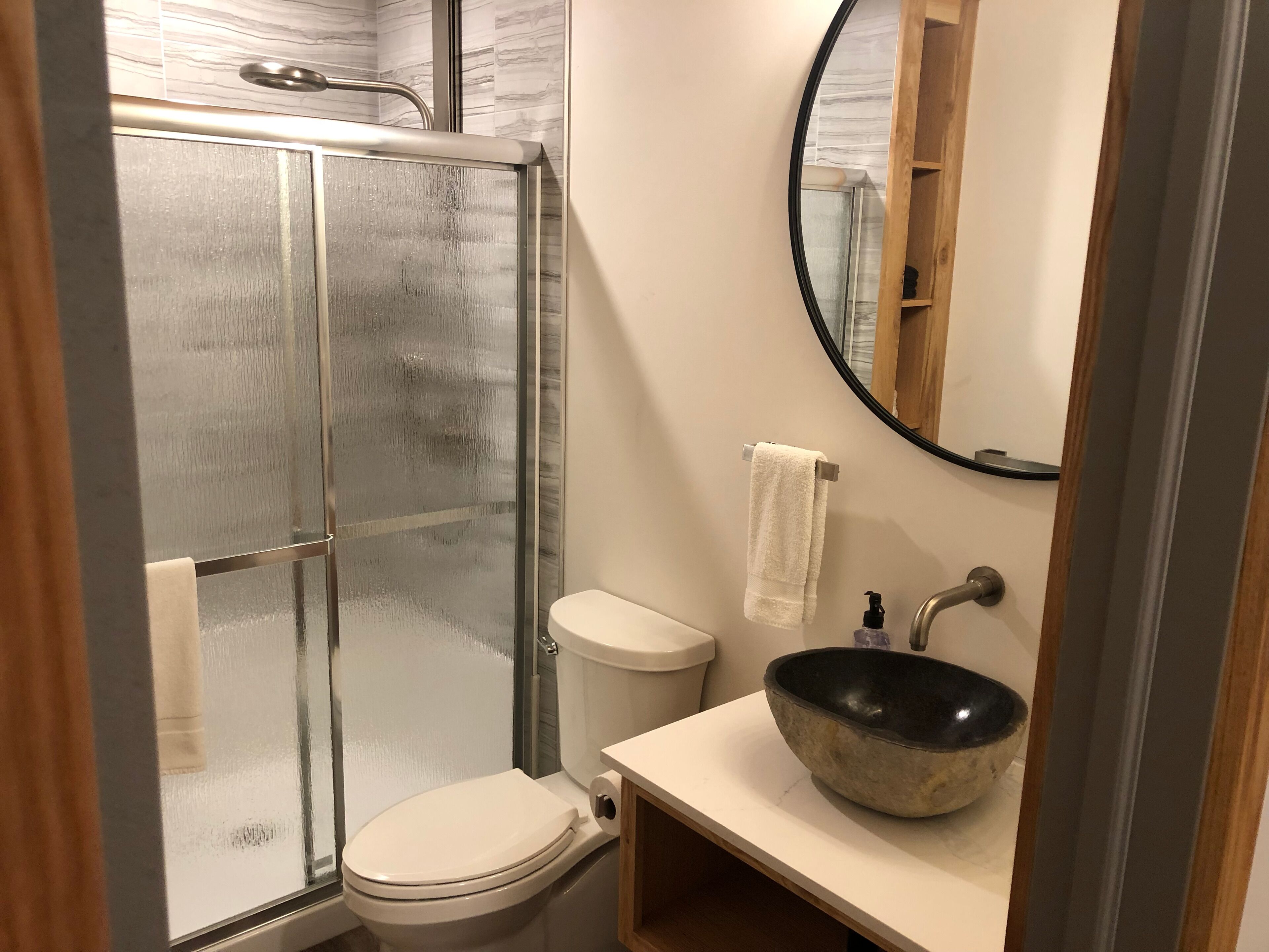 A bathroom with a glass-enclosed shower, a toilet, a sink with a stone basin, and a mirror.