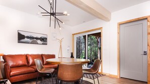 Een moderne eetruimte met een ronde tafel, een leren bank en uitzicht op een bos door grote ramen.