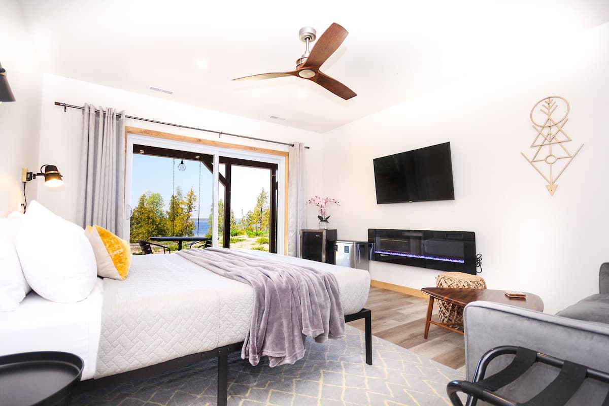Een moderne slaapkamer met een bed, een plafondventilator, een televisie en uitzicht op de omgeving.
