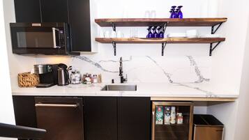 A modern kitchen with a built-in microwave, stainless steel appliances, a marble backsplash, and wooden shelves above the countertop.
