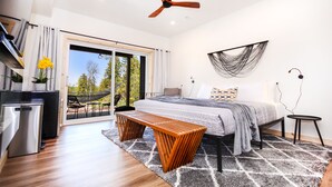 Een moderne slaapkamer met een bed, een bankje, een plafondventilator en uitzicht op de omgeving.