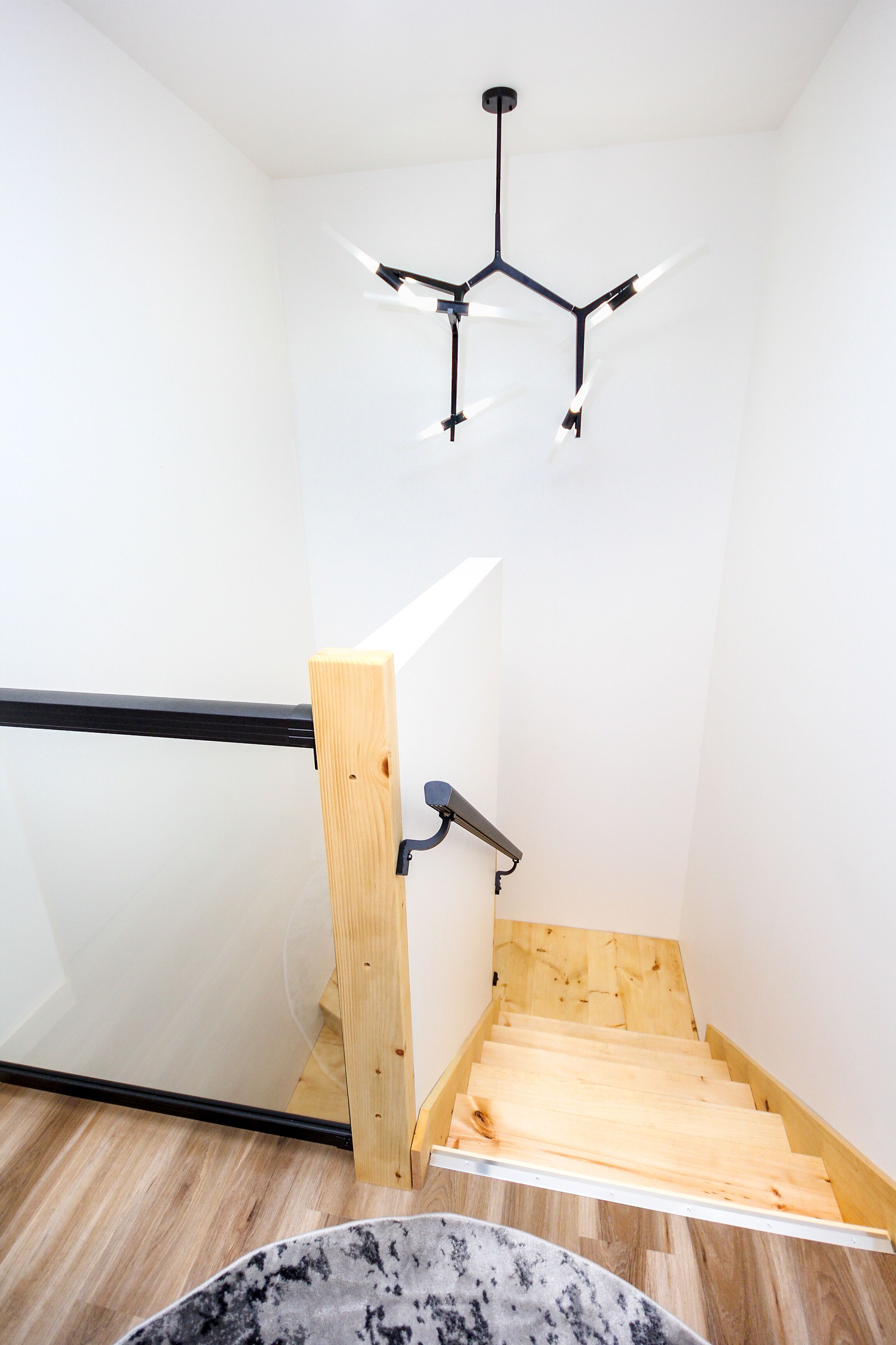 A staircase with a wooden handrail and a modern light fixture above.