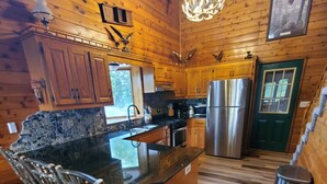 Interior de una cabaña de madera con cocina que cuenta con encimeras de granito, una isla central con taburetes de bar y un refrigerador de acero inoxidable.