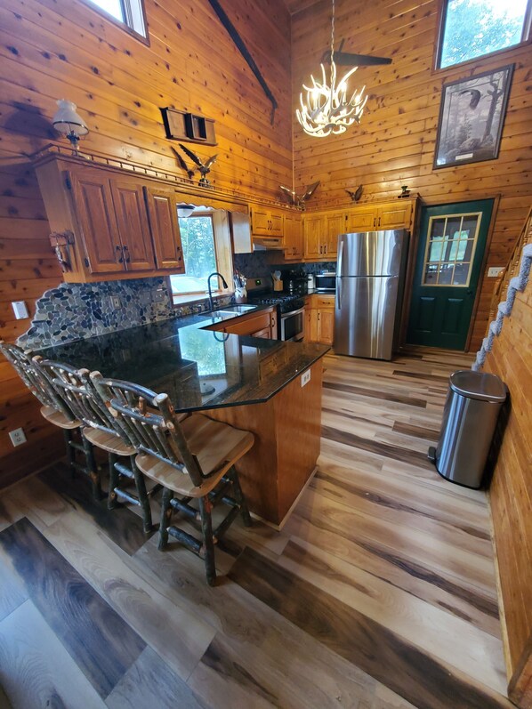 L'intérieur d'une cabane en bois comprend une cuisine dotée de plans de travail en granit, d'un îlot central avec des tabourets de bar et d'un réfrigérateur en acier inoxydable.
