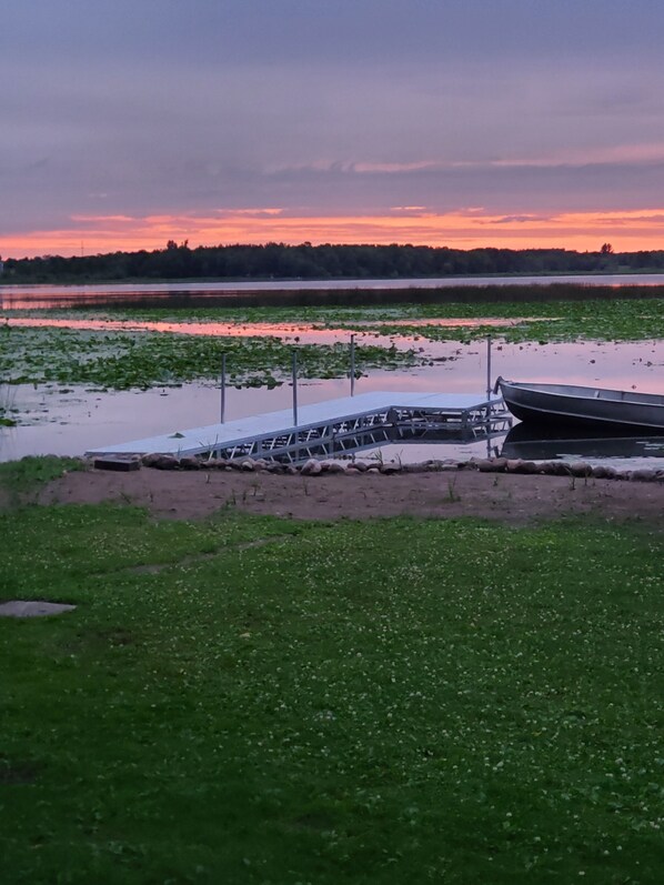 A boat docked at a pier with a grassy foreground and a sunset in the background. - Relax and Enjoy fishing and wildlife on Goose lake (Stanchfield)