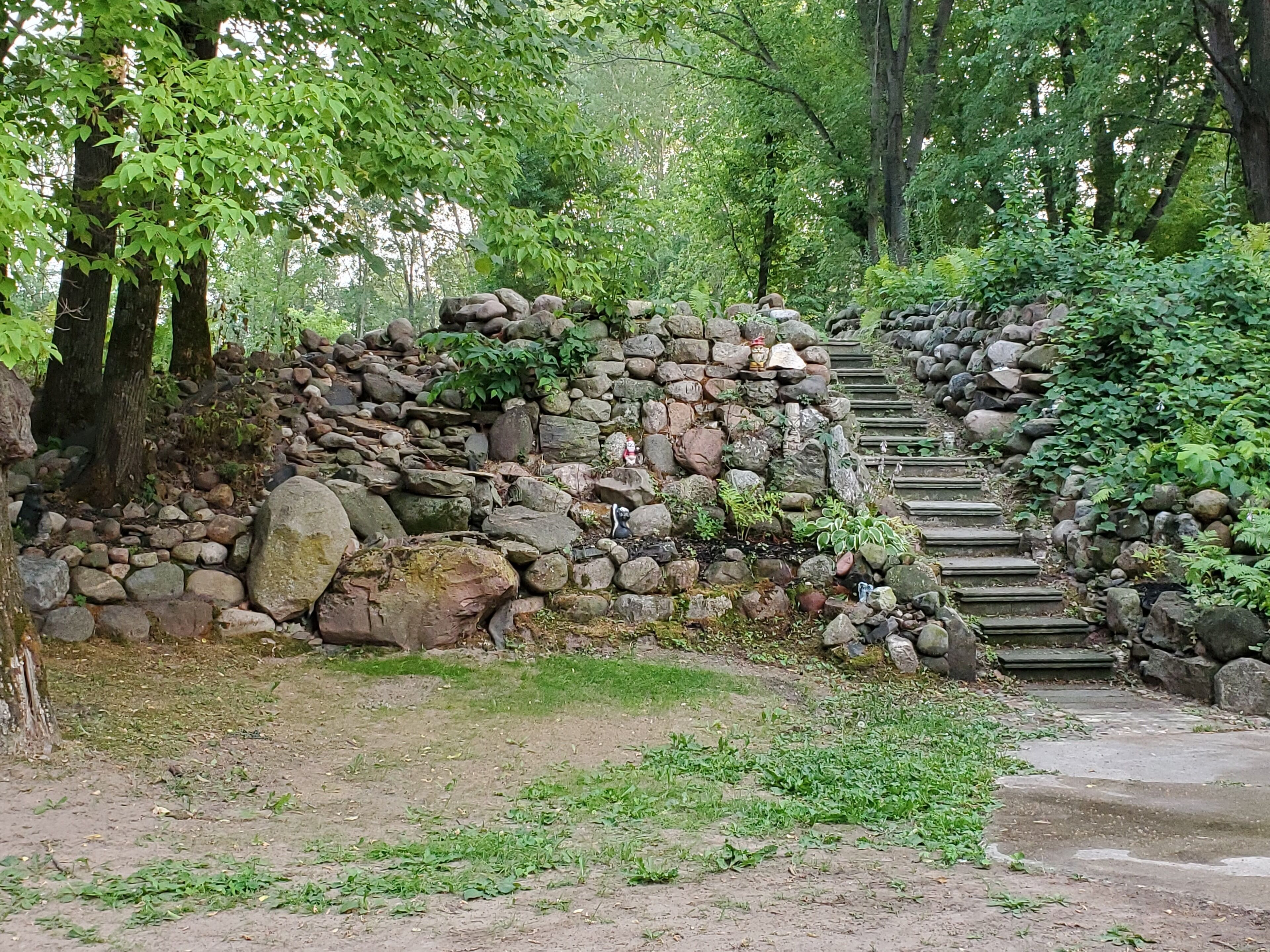 Una escalera de piedra en un área boscosa, con peldaños que ascienden hacia un muro rocoso.