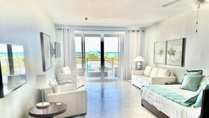 Habitación de hotel con balcón, cama, sofá, sillón y una mesita.